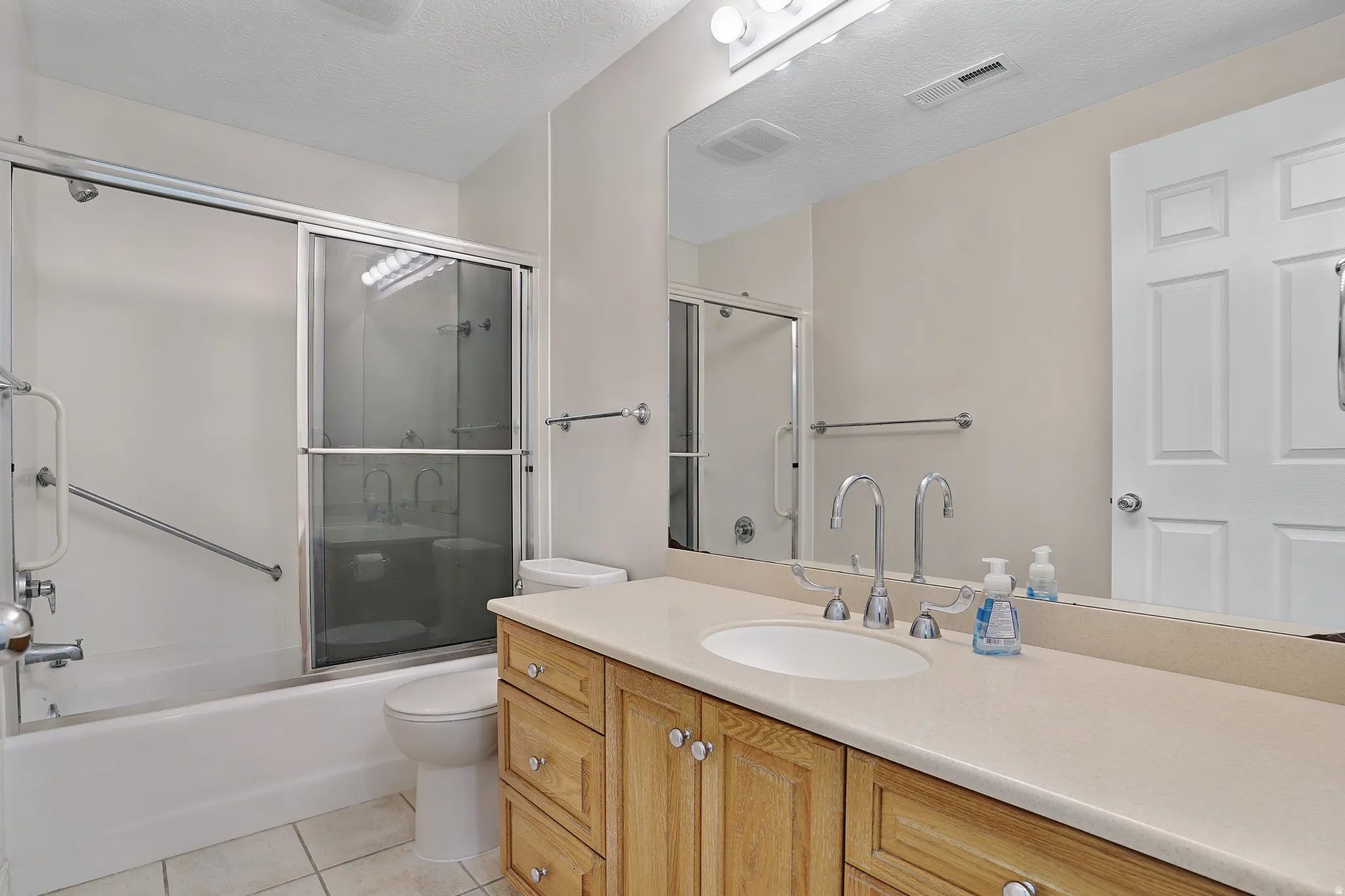 Full bath with vanity, light tile patterned flooring, enclosed tub / shower combo, and a textured ceiling
