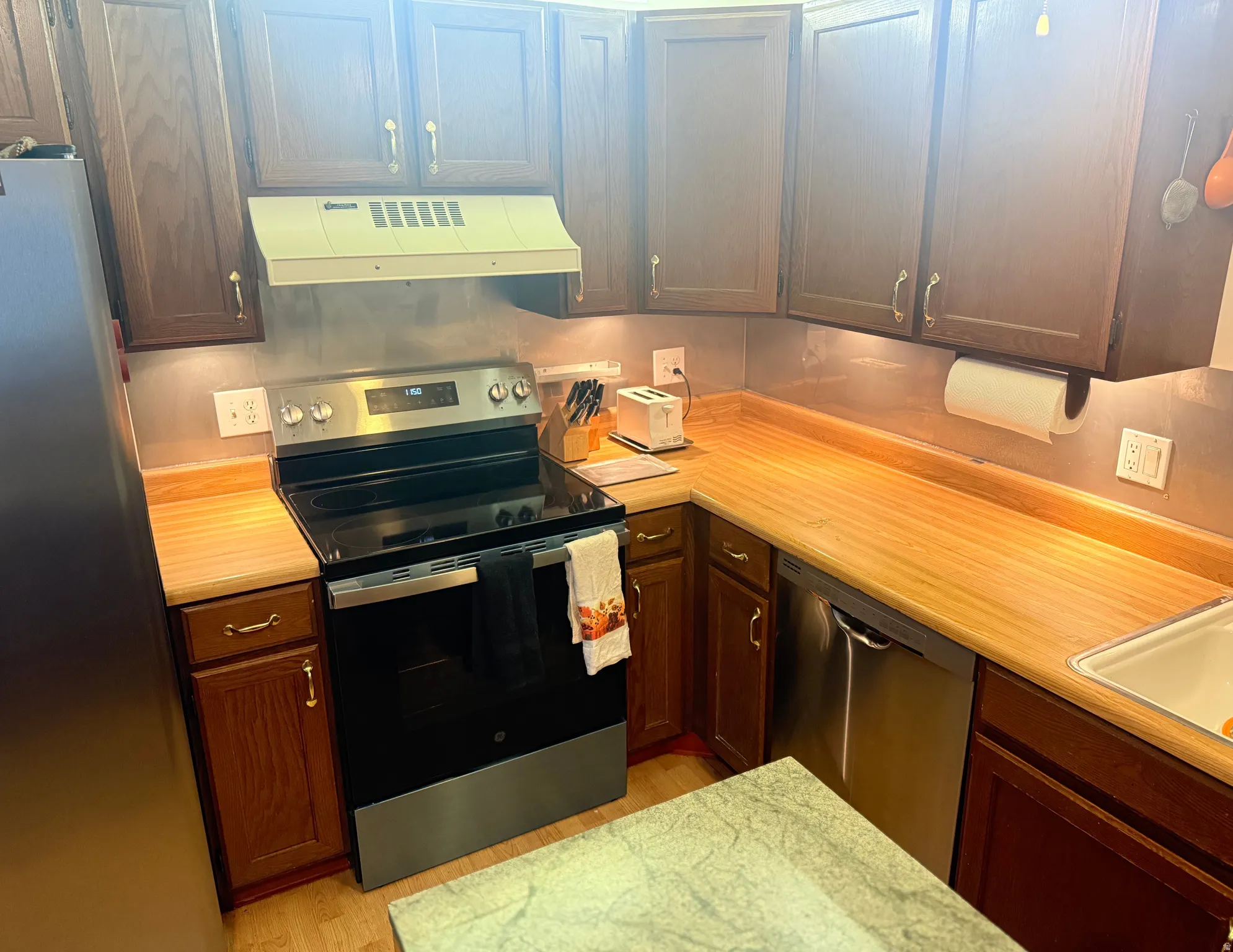 Kitchen featuring stainless steel appliances, light countertops, exhaust hood, and dark wood finish cabinetry