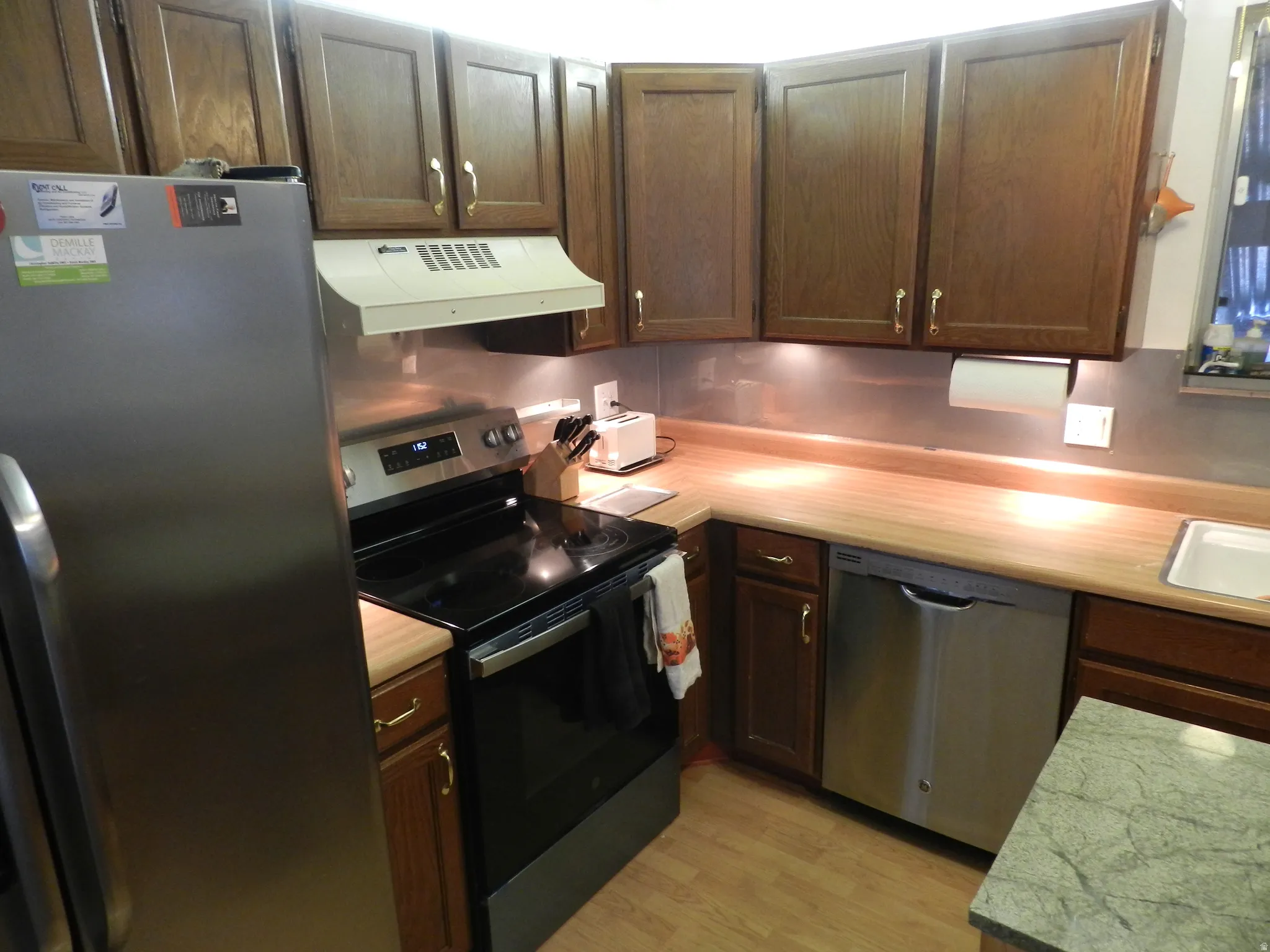 Kitchen with stainless steel appliances, dark wood finish cabinetry, light countertops, and extractor fan