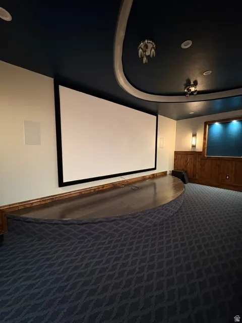 Home theater room with dark carpet, wood walls, a wainscoted wall, and a tray ceiling