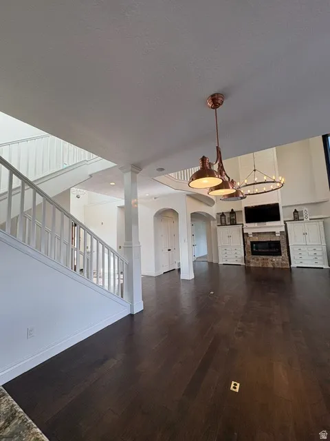 Unfurnished living room featuring dark wood-style floors, a fireplace, arched walkways, a chandelier, and a textured ceiling