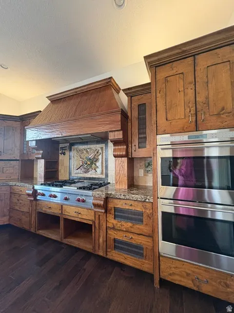 Kitchen featuring stainless steel appliances, dark wood-style floors, wood finish cabinetry, dark stone countertops, and a textured ceiling