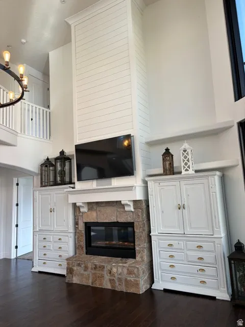 Living room featuring a stone fireplace, dark wood-style floors, a high ceiling, and a chandelier