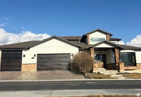 View of front of house featuring stone siding, a garage, driveway, and covered porch