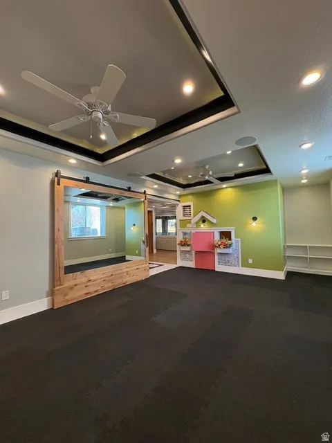 Misc room featuring a barn door, a tray ceiling, recessed lighting, and ceiling fan
