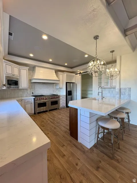 Two tone kitchen with backsplash, a barn door, light stone countertops, dark wood-type flooring, and stainless steel appliances