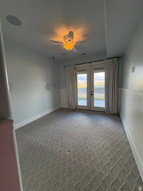 Unfurnished room with french doors, light colored carpet, a wainscoted wall, and ceiling fan