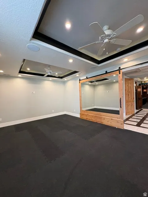 Unfurnished room featuring a barn door, a tray ceiling, ceiling fan, recessed lighting, and carpet flooring