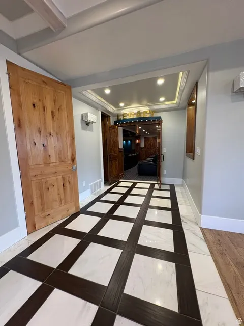 Hallway with a tray ceiling, recessed lighting, inlaid floor details, and crown molding