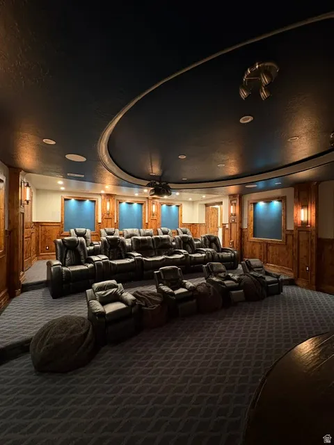 Carpeted home theater room with wooden walls, wainscoting, a ceiling fan, and a raised ceiling