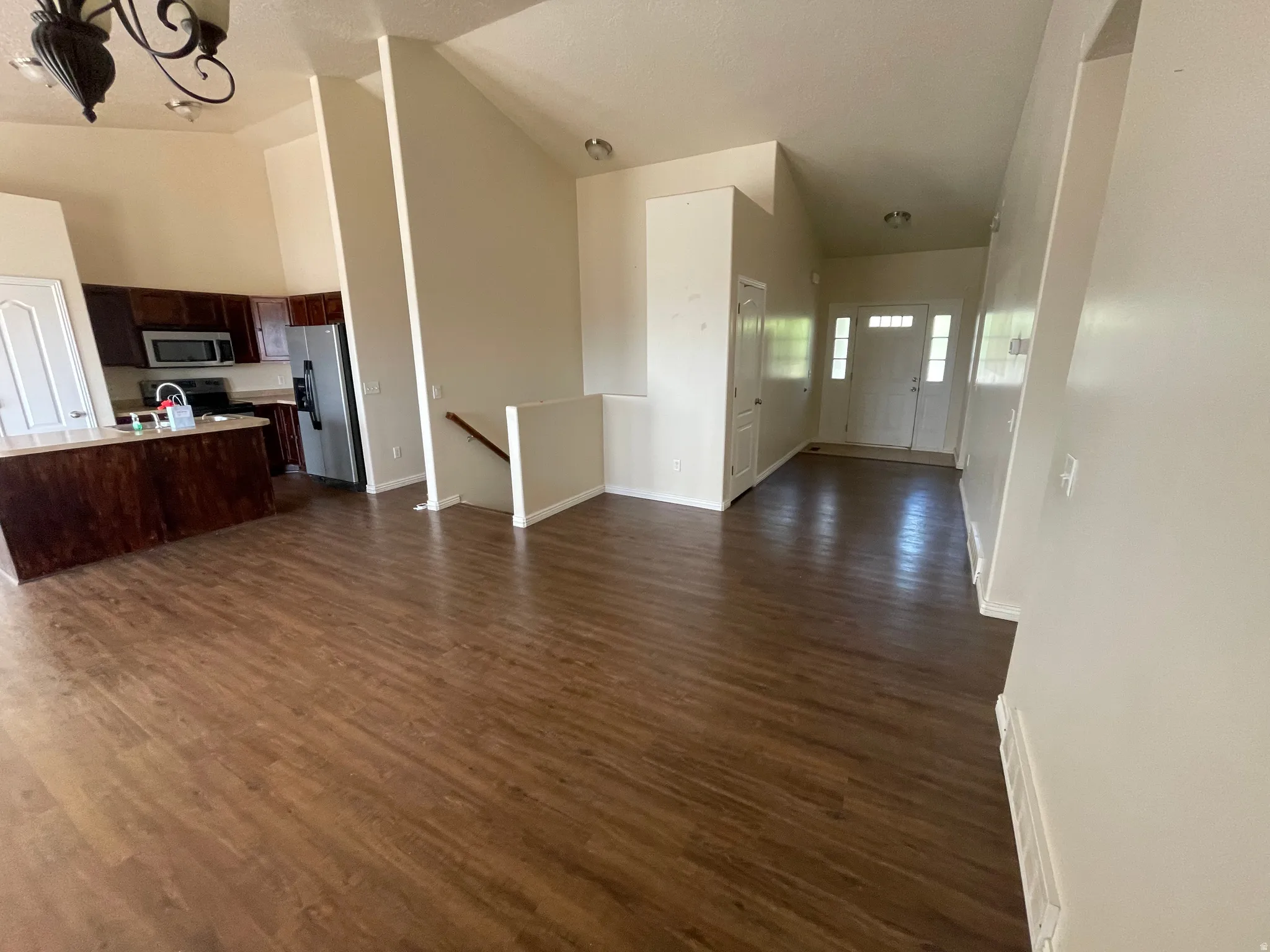 Open-concept living area featuring wood-finish flooring, vaulted ceilings, and a kitchen with dark wood cabinetry