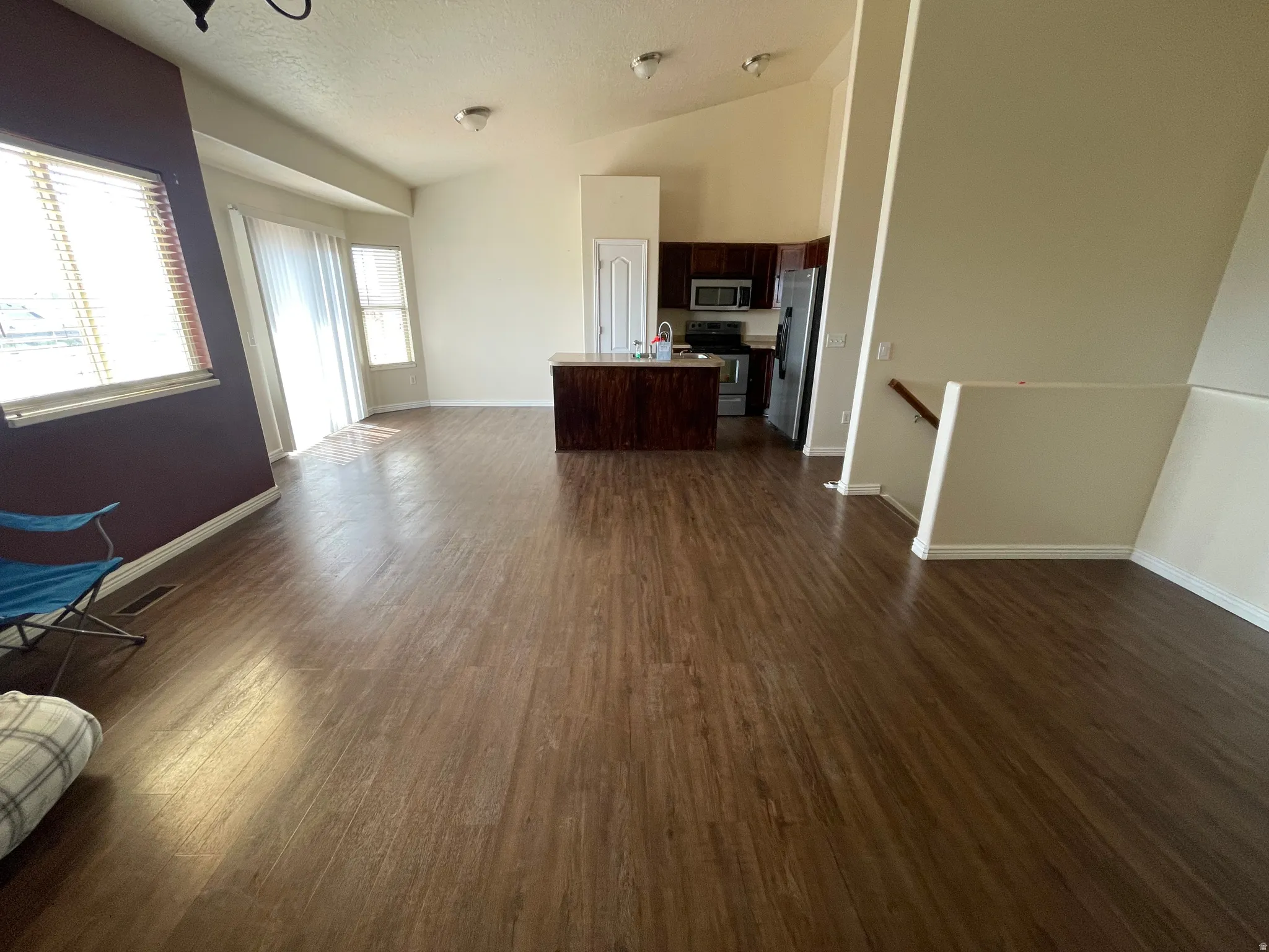 Spacious open-concept living area featuring wood-finish flooring, vaulted ceilings, and a kitchen with dark cabinetry and stainless steel appliances