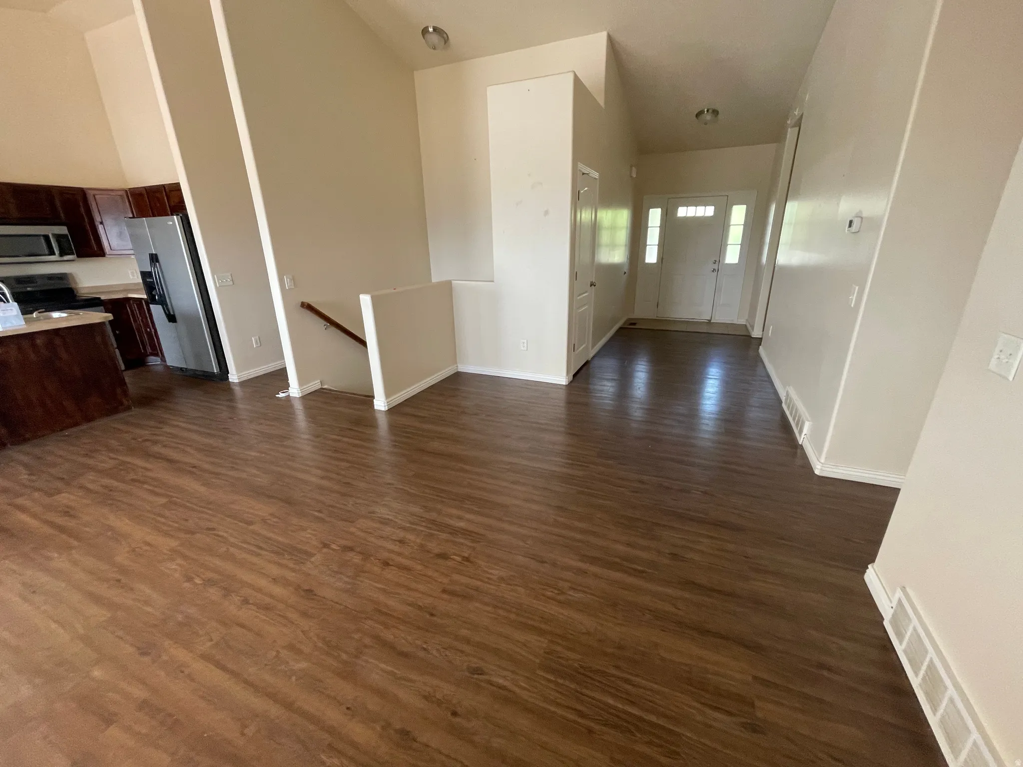 Open-concept living space featuring wood-finish flooring, vaulted ceilings, and a kitchen with dark cabinetry