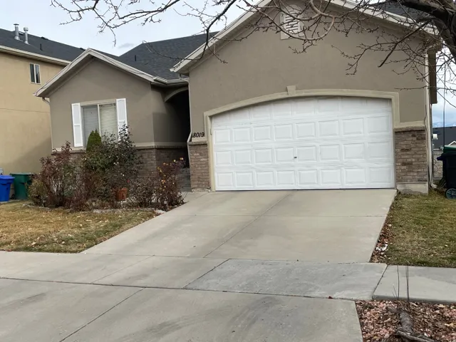 View of front of home with stucco siding, driveway, a garage, roof with shingles, and brick siding