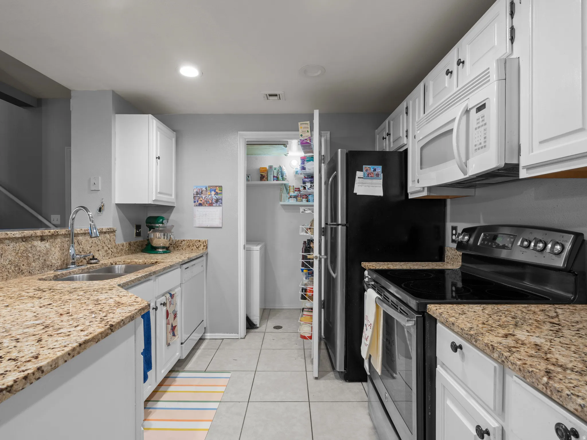 Kitchen featuring white appliances, light stone countertops, white cabinetry, light tile patterned flooring, and recessed lighting