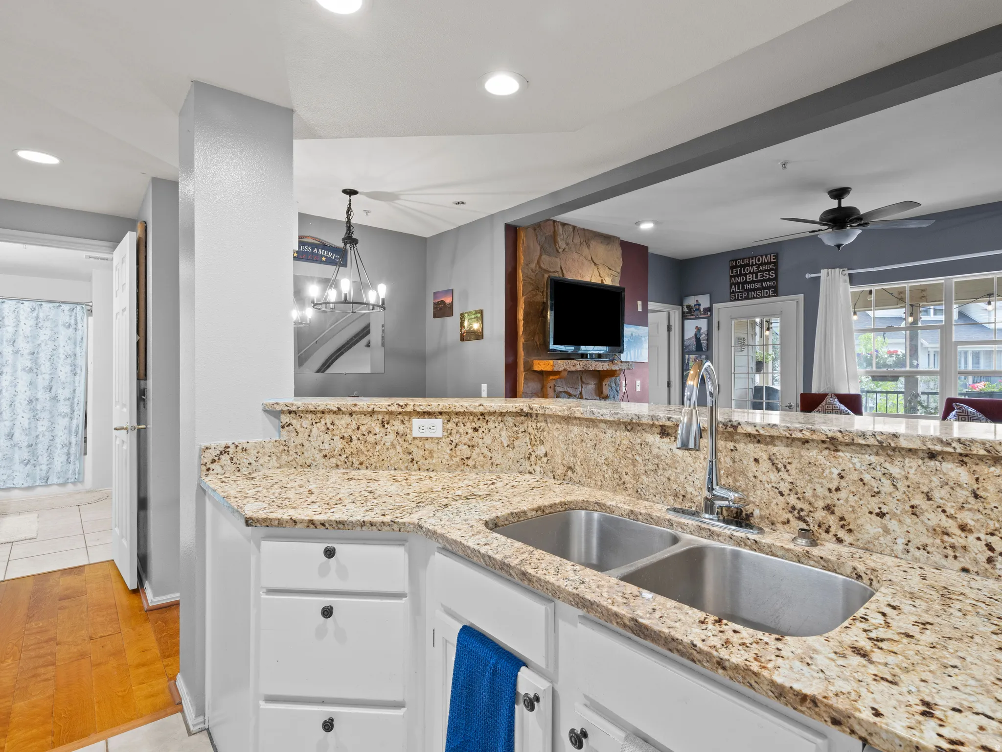 Kitchen with light stone counters, white cabinets, open floor plan, ceiling fan, and light wood-type flooring