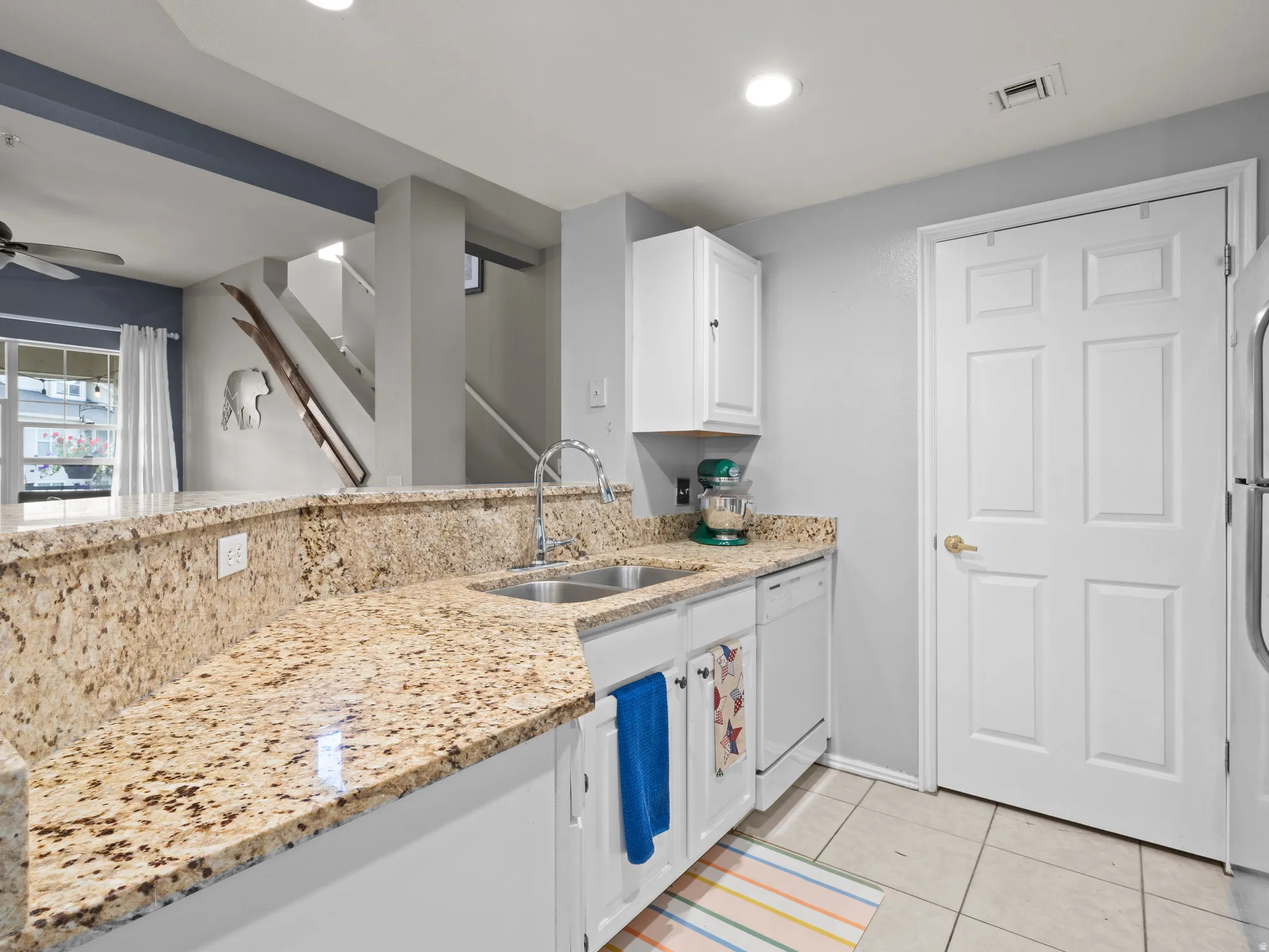 Kitchen featuring white cabinetry, ceiling fan, dishwasher, light stone countertops, and light tile patterned floors