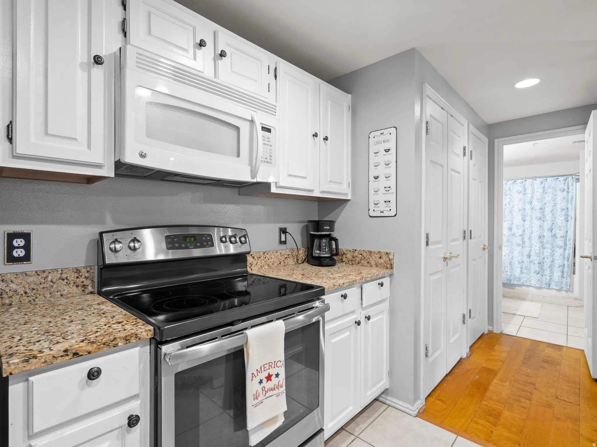 Kitchen featuring stainless steel range with electric stovetop, light tile patterned floors, white microwave, white cabinets, and recessed lighting