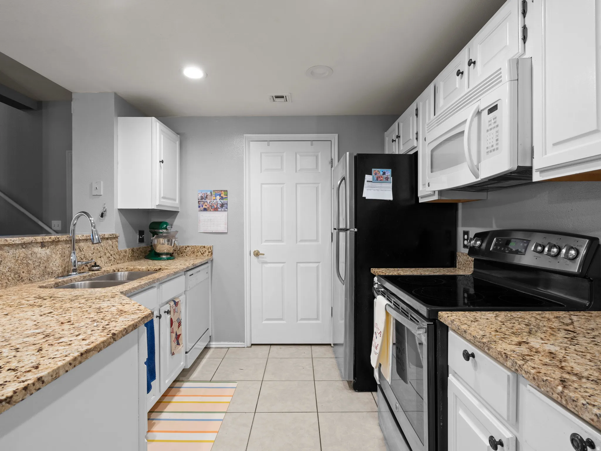 Kitchen with white appliances, light stone countertops, white cabinets, light tile patterned floors, and recessed lighting