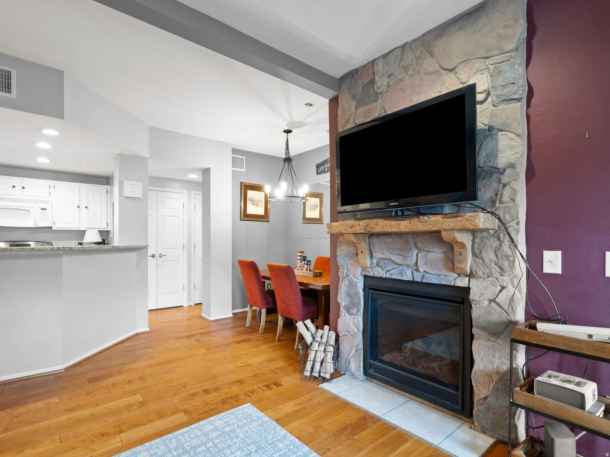 Living area featuring light wood-type flooring, hanging lights, and a stone fireplace