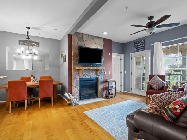 Living room with a stone fireplace, light wood-style floors, suspended lighting, and a ceiling fan