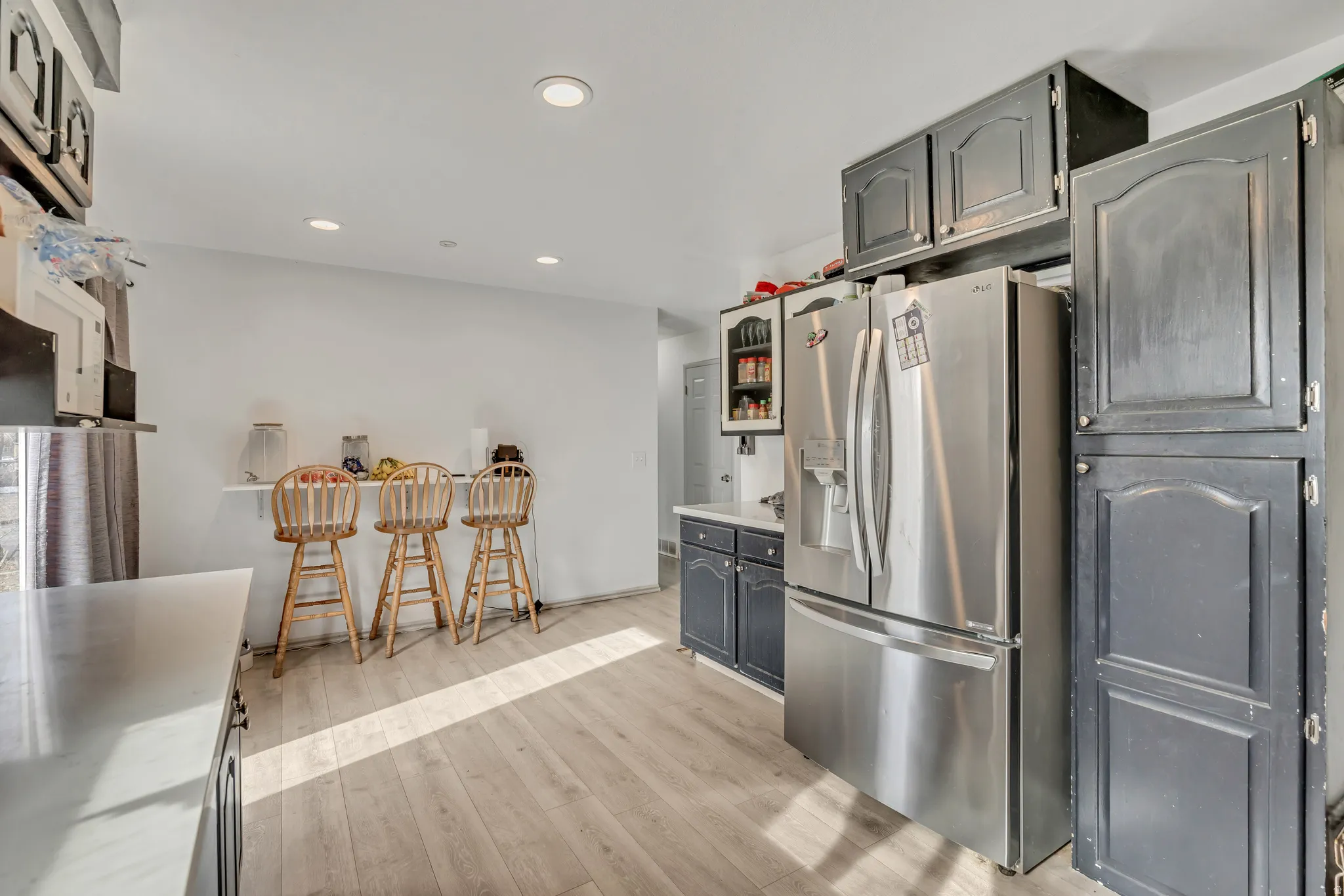 Kitchen featuring stainless steel fridge, light wood-style floors, recessed lighting, gray cabinets, and glass insert cabinets