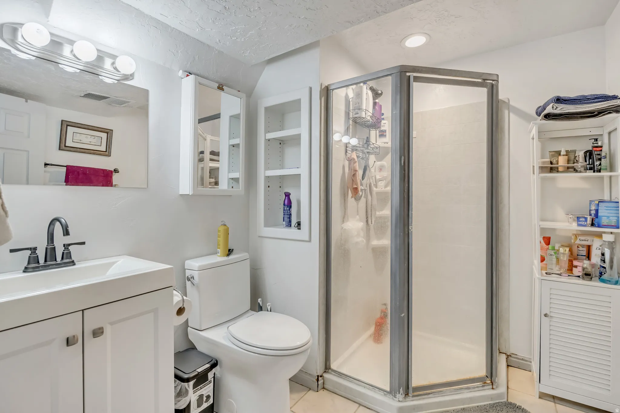 Bathroom with a shower stall, vanity, a textured ceiling, and light tile patterned floors