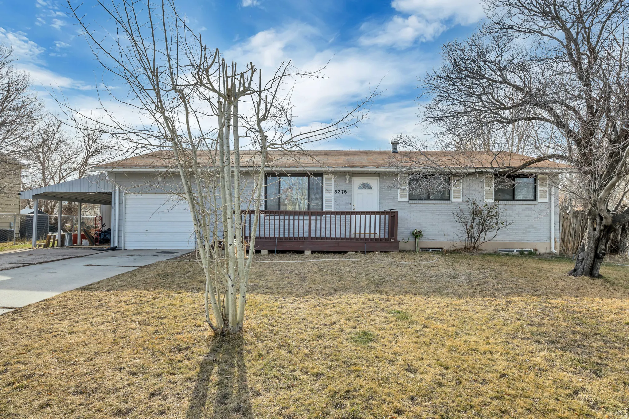 Ranch-style home with brick siding, a front lawn, an attached carport, driveway, and a deck