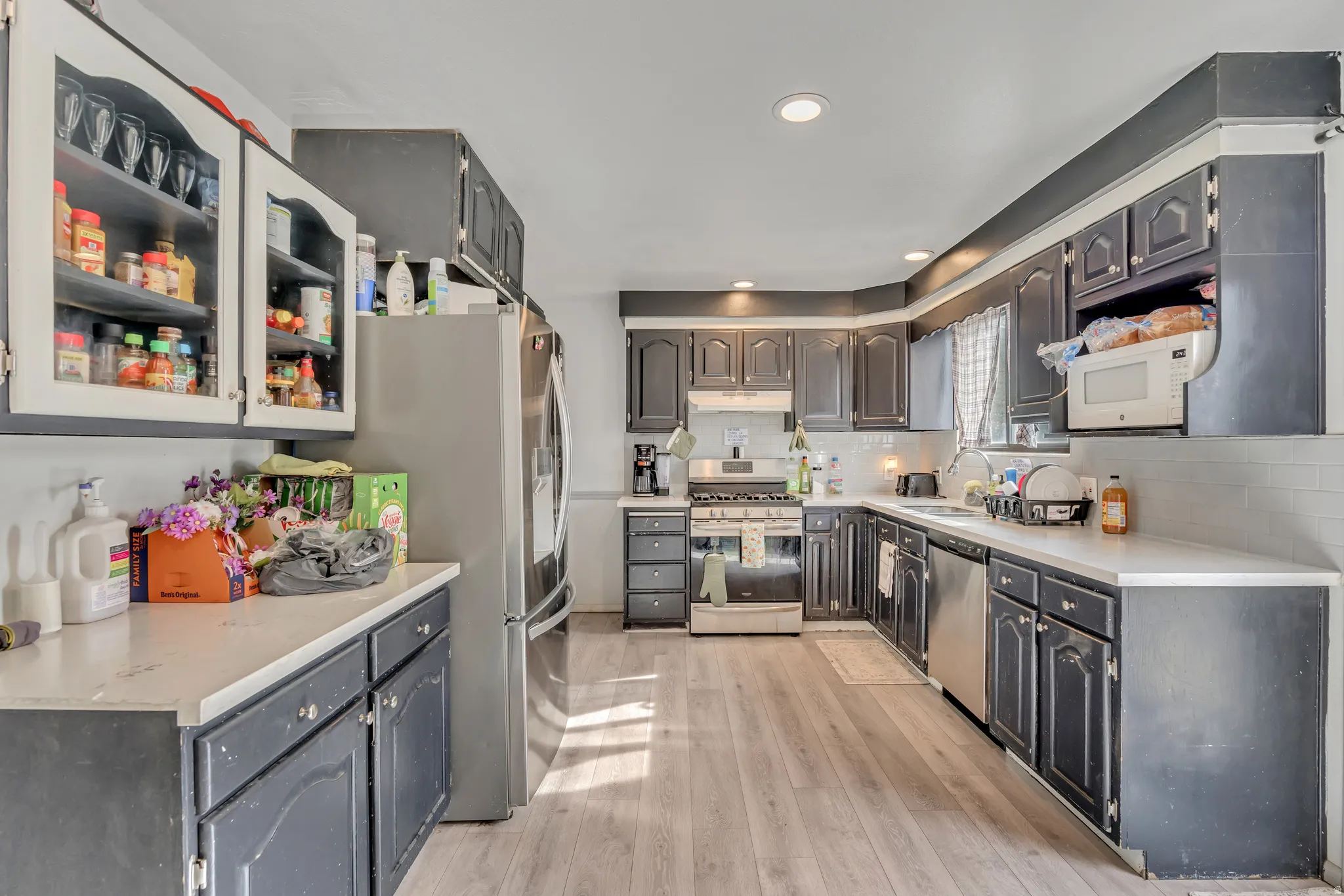 Kitchen with stainless steel appliances, light wood-style floors, backsplash, glass fronted cabinets, and recessed lighting