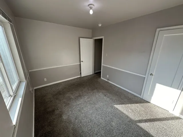 Unfurnished bedroom with dark colored carpet and baseboards