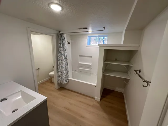 Bathroom featuring double vanity, a textured ceiling, light wood finished floors, shower / bath combo with shower curtain, and a closet