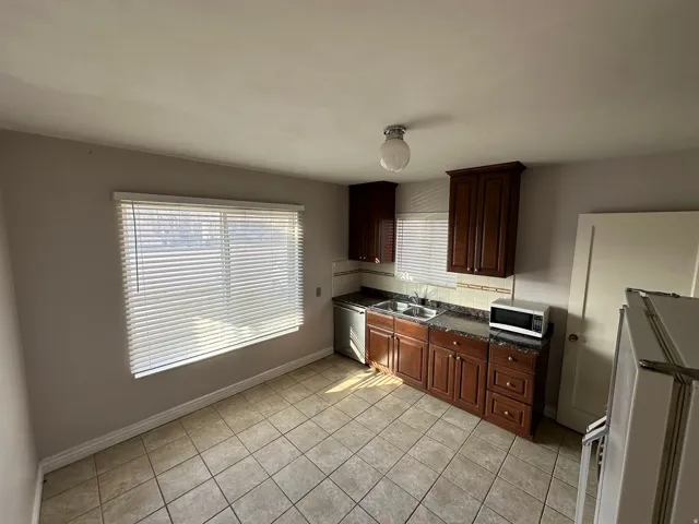 Kitchen with stainless steel appliances, light tile patterned flooring, decorative backsplash, and dark wood finish cabinets
