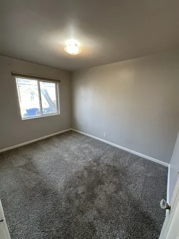 Unfurnished room featuring dark colored carpet and baseboards