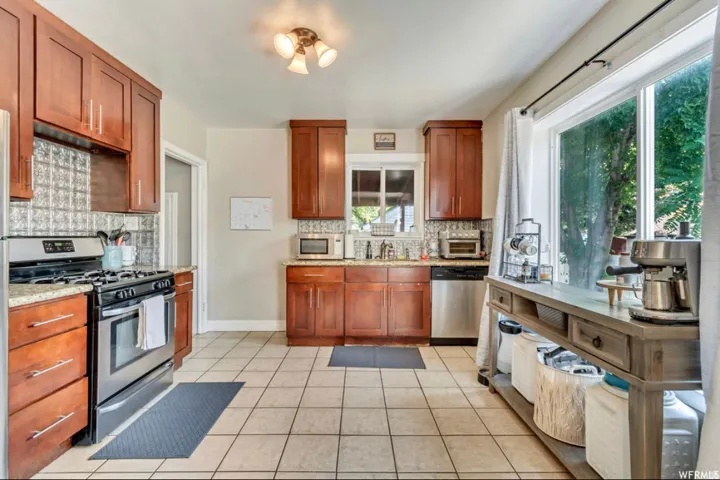 Kitchen featuring stainless steel appliances, light tile patterned floors, wood finish cabinetry, and light stone countertops