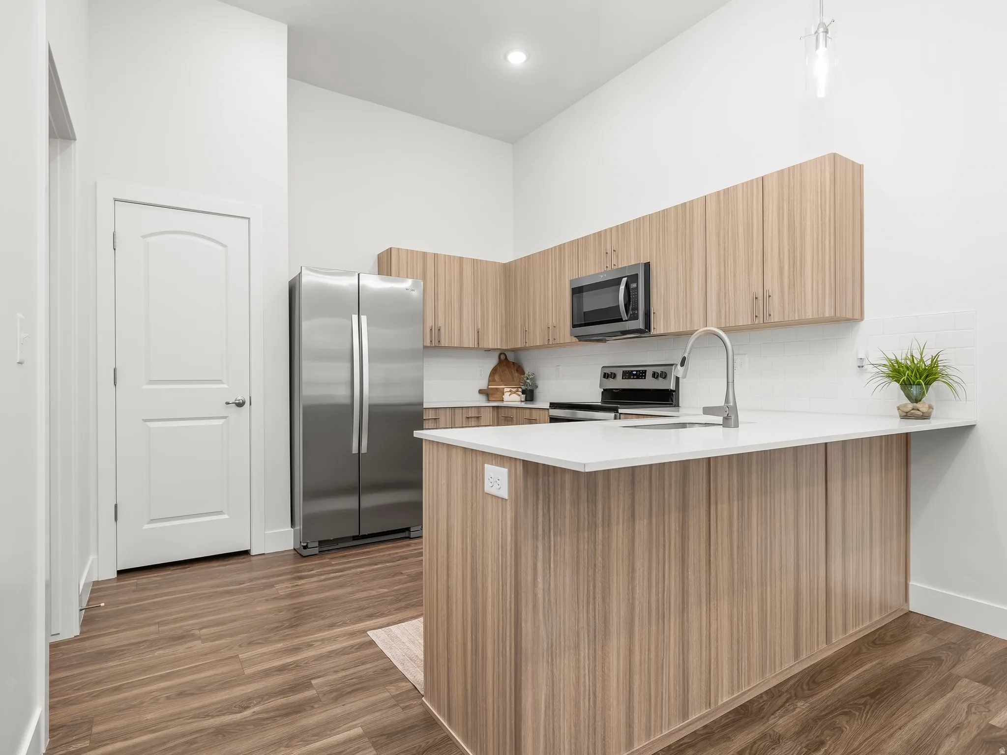 Modern kitchen with midtone cabinets, quartz counter, tile backsplash, and pendant lighting. *Fridge not included.