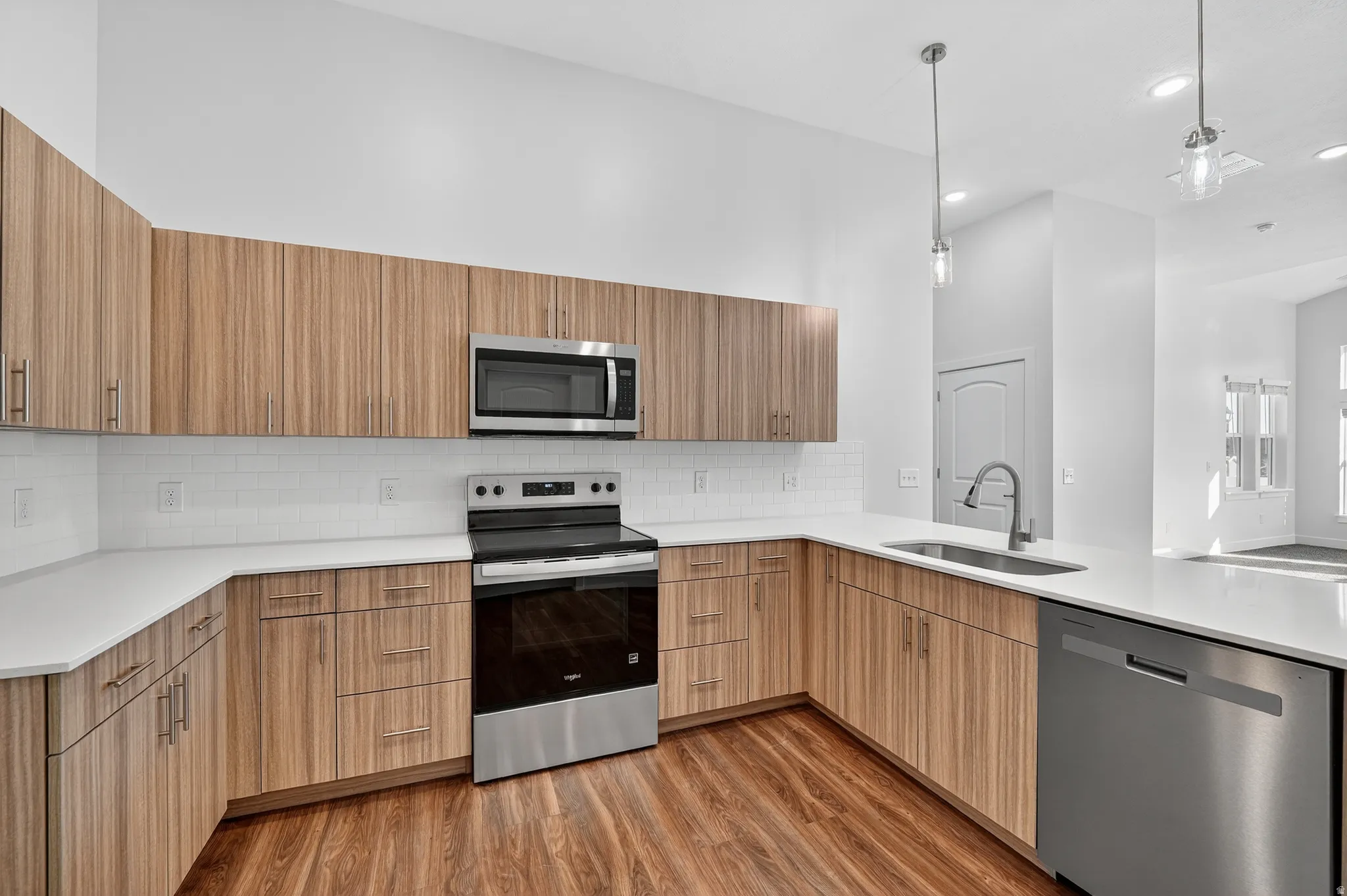 Modern kitchen with midtone cabinets, quartz counter, tile backsplash, and pendant lighting. *Fridge not included.