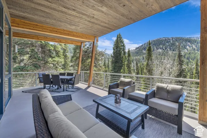 View of covered deck featuring a outdoor lounge area, surrounded by large pine trees, and mountain views