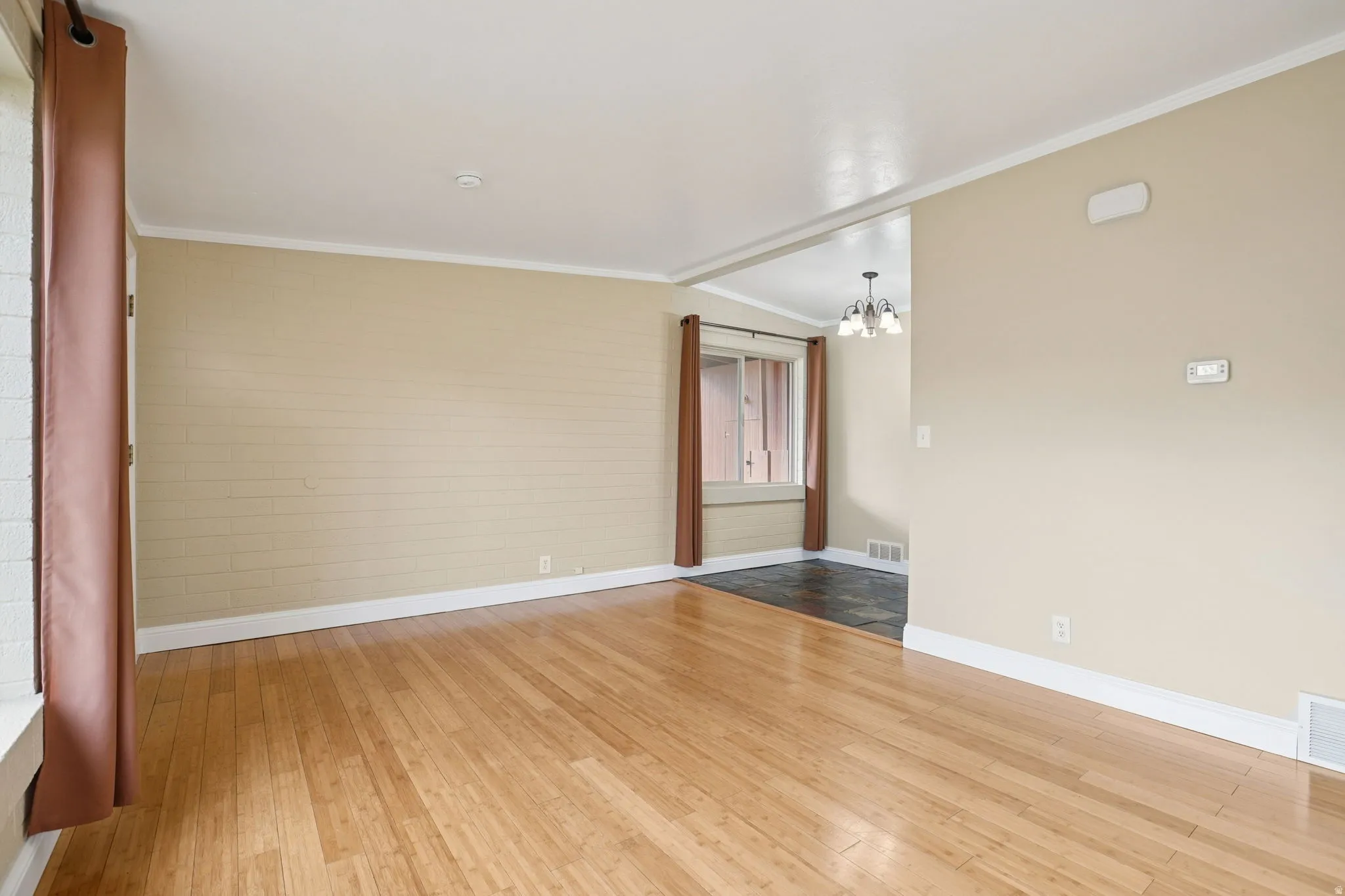Empty room with ornamental molding, light wood-type flooring, suspended lighting, and lofted ceiling