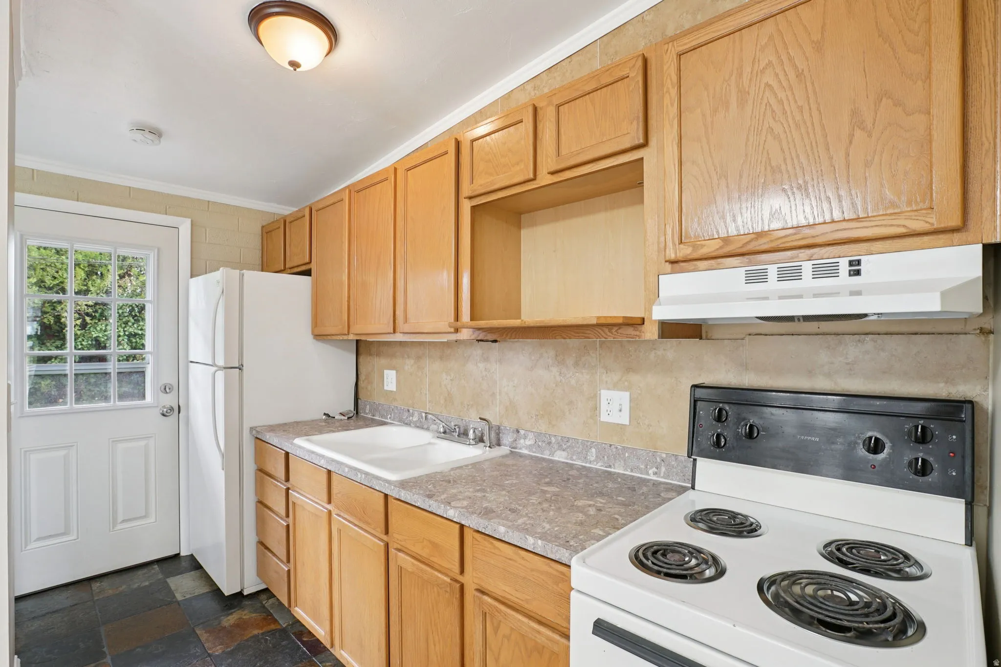 Kitchen with white appliances, ornamental molding, light wood finish cabinets, slate flooring, and light countertops