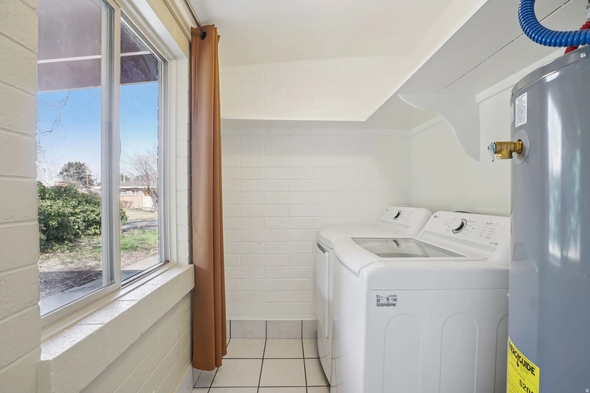 Laundry area featuring water heater, new washing machine and new dryer, light tile patterned floors, and tile walls
