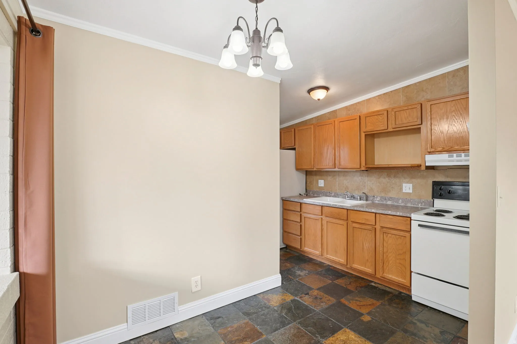 Kitchen featuring white appliances, dark stone finish floors, light countertops, ornamental molding, and a chandelier