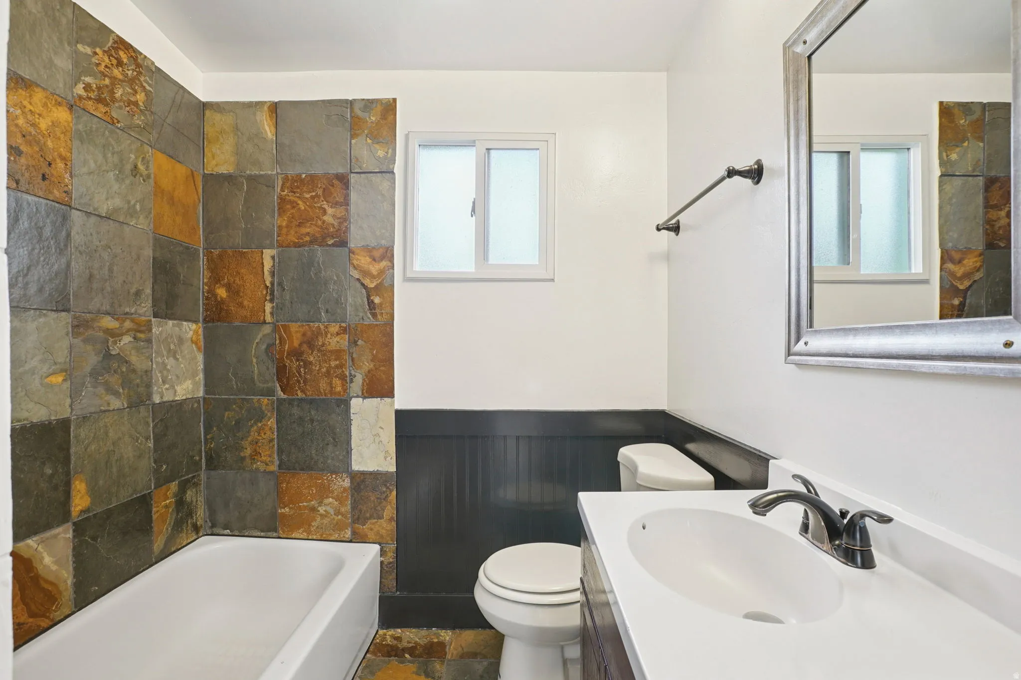 Updated bathroom featuring wainscoting, slate tile floors, vanity, and a tub