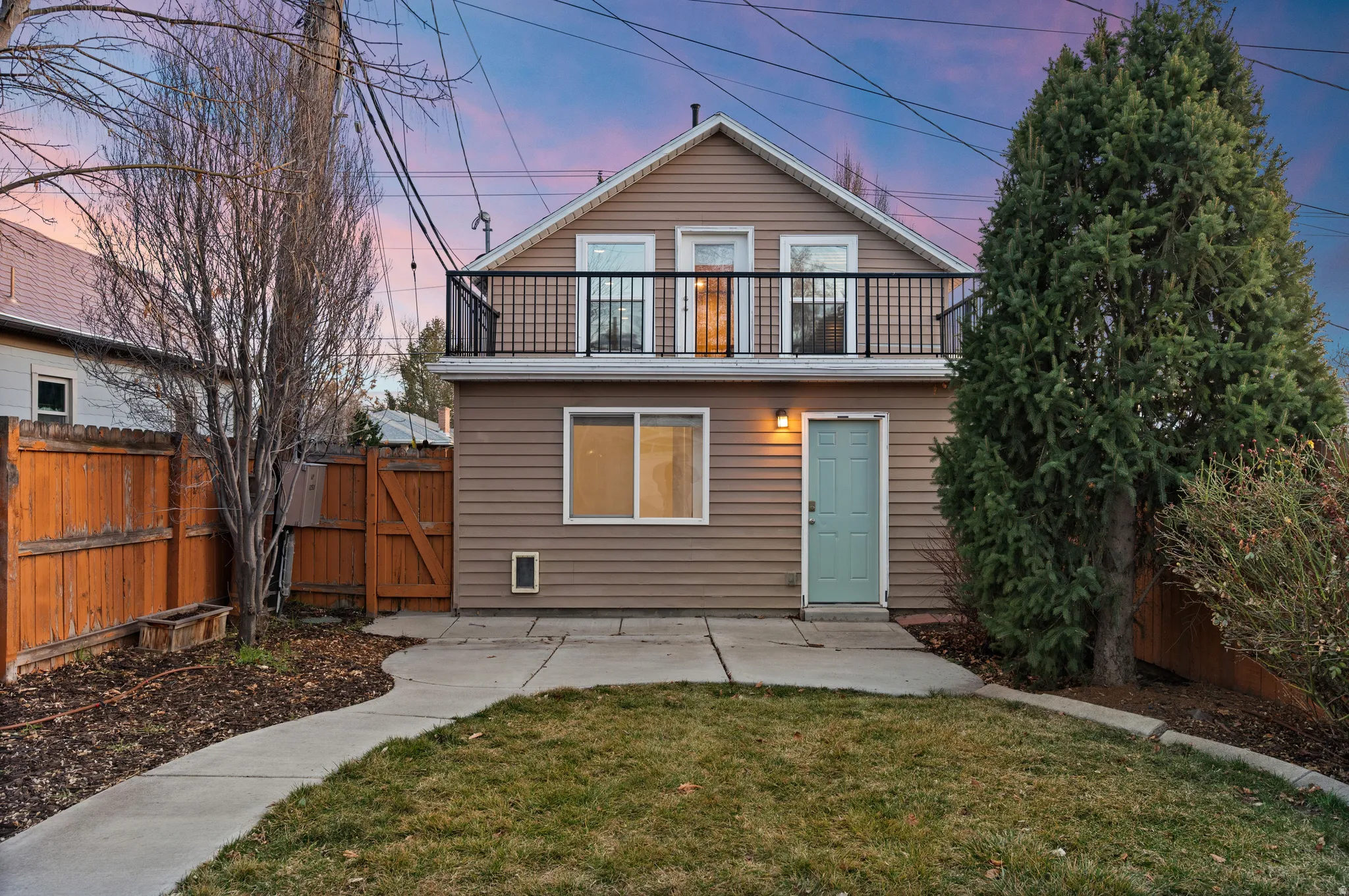 Back of property at dusk featuring a fenced backyard, a patio, a gate, and a balcony