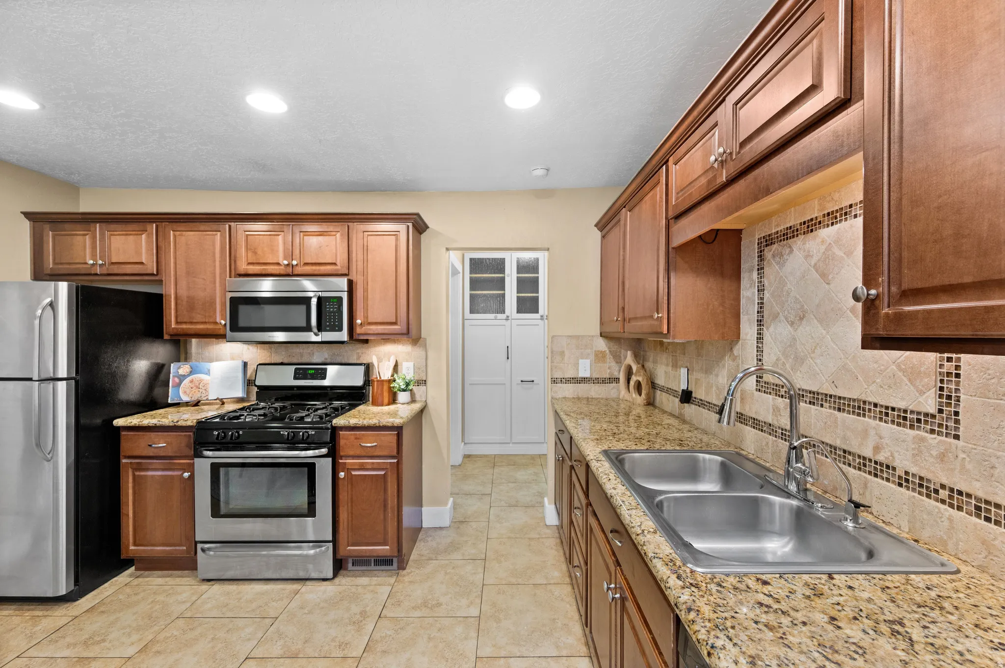 Kitchen featuring stainless steel appliances, wood finish cabinetry, light stone counters, light tile patterned floors, and tasteful backsplash