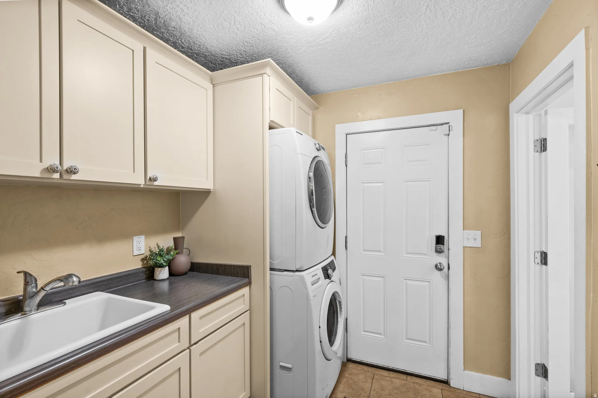 Laundry room featuring stacked washing machine and dryer, cabinet space, a textured ceiling, and light tile patterned floors