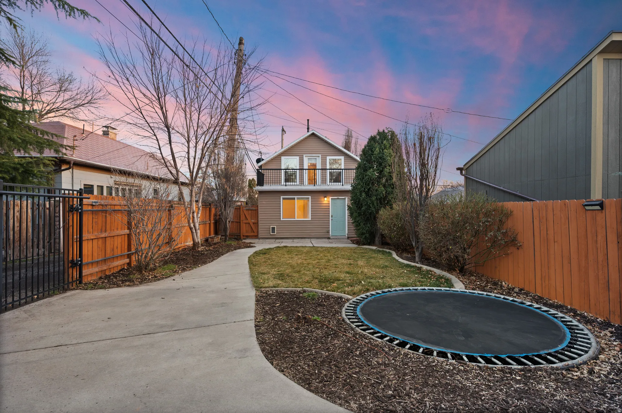 Back of house at dusk with a fenced backyard, a trampoline, a gate, and a patio
