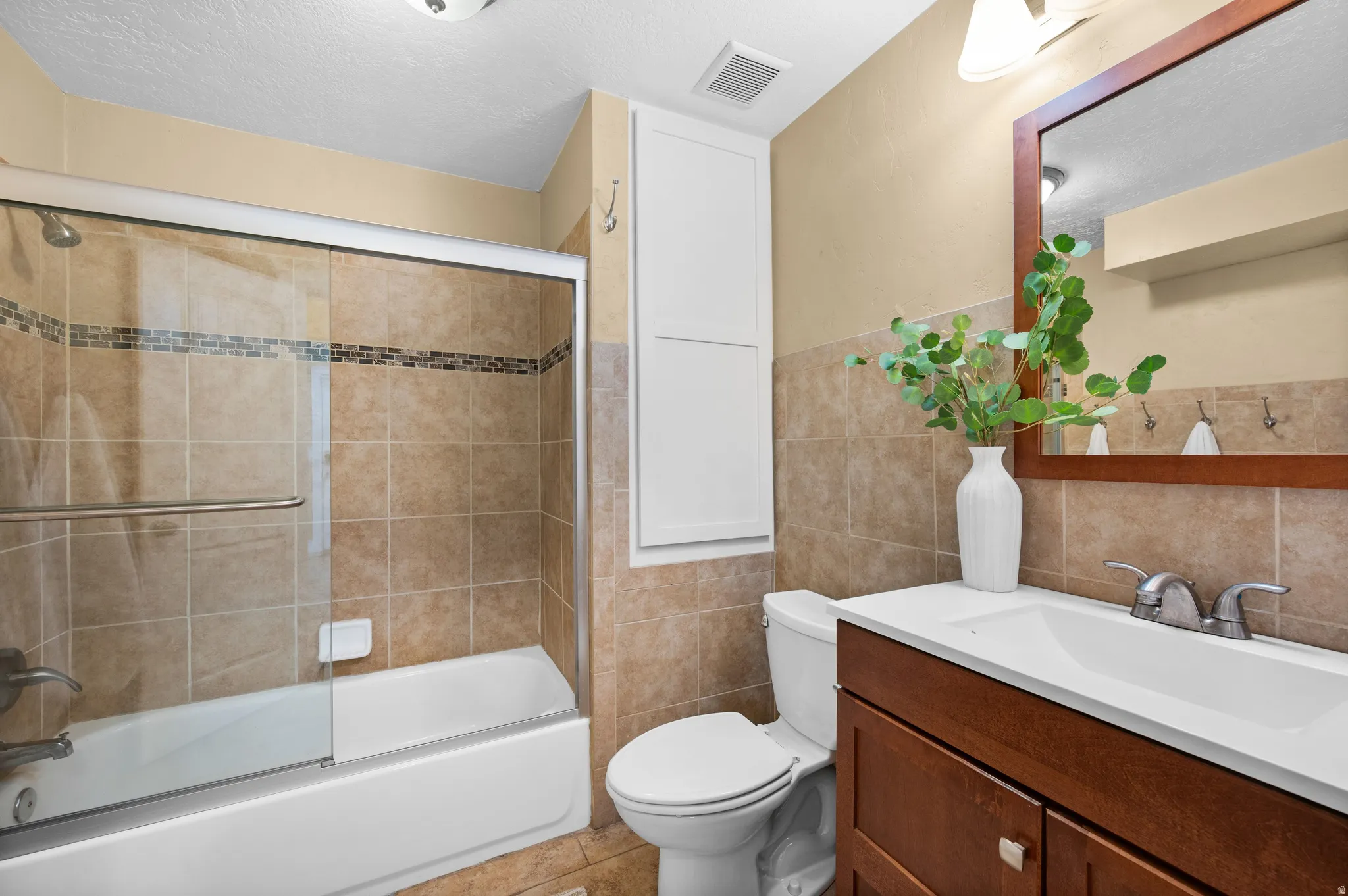 Bathroom with vanity, tile walls, enclosed tub / shower combo, and a textured ceiling