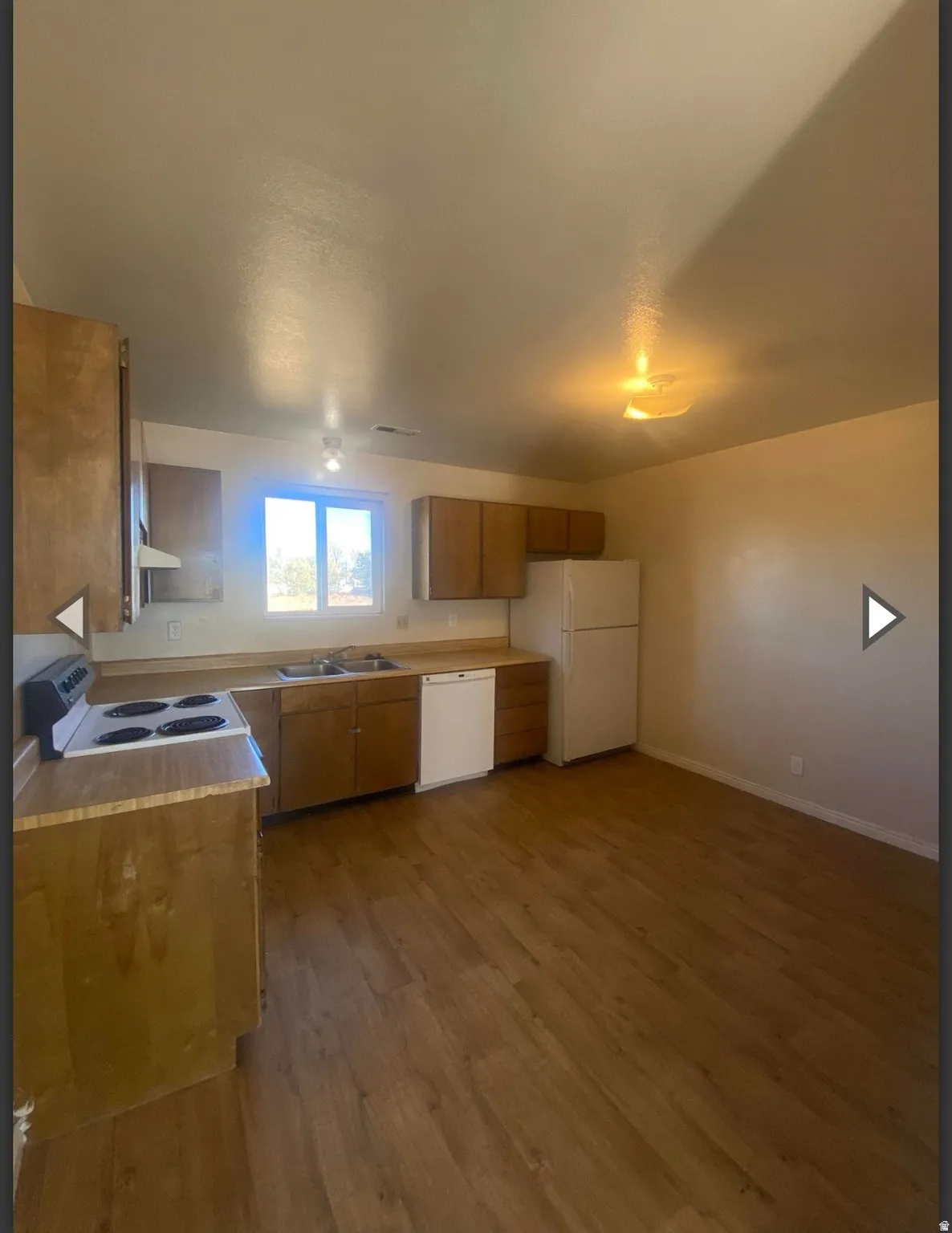 Kitchen featuring wood finish cabinets, light countertops, white appliances, and dark wood-type flooring