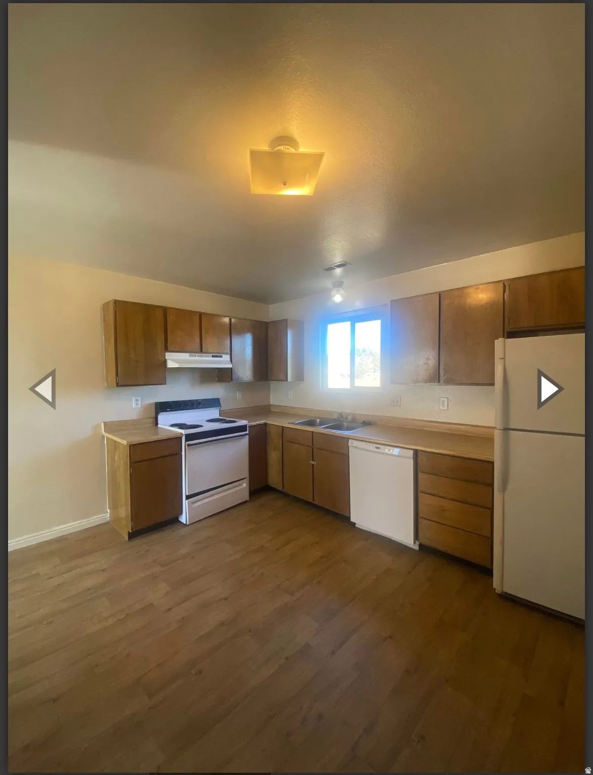 Kitchen featuring white appliances, light countertops, wood finish cabinets, and dark wood finished floors