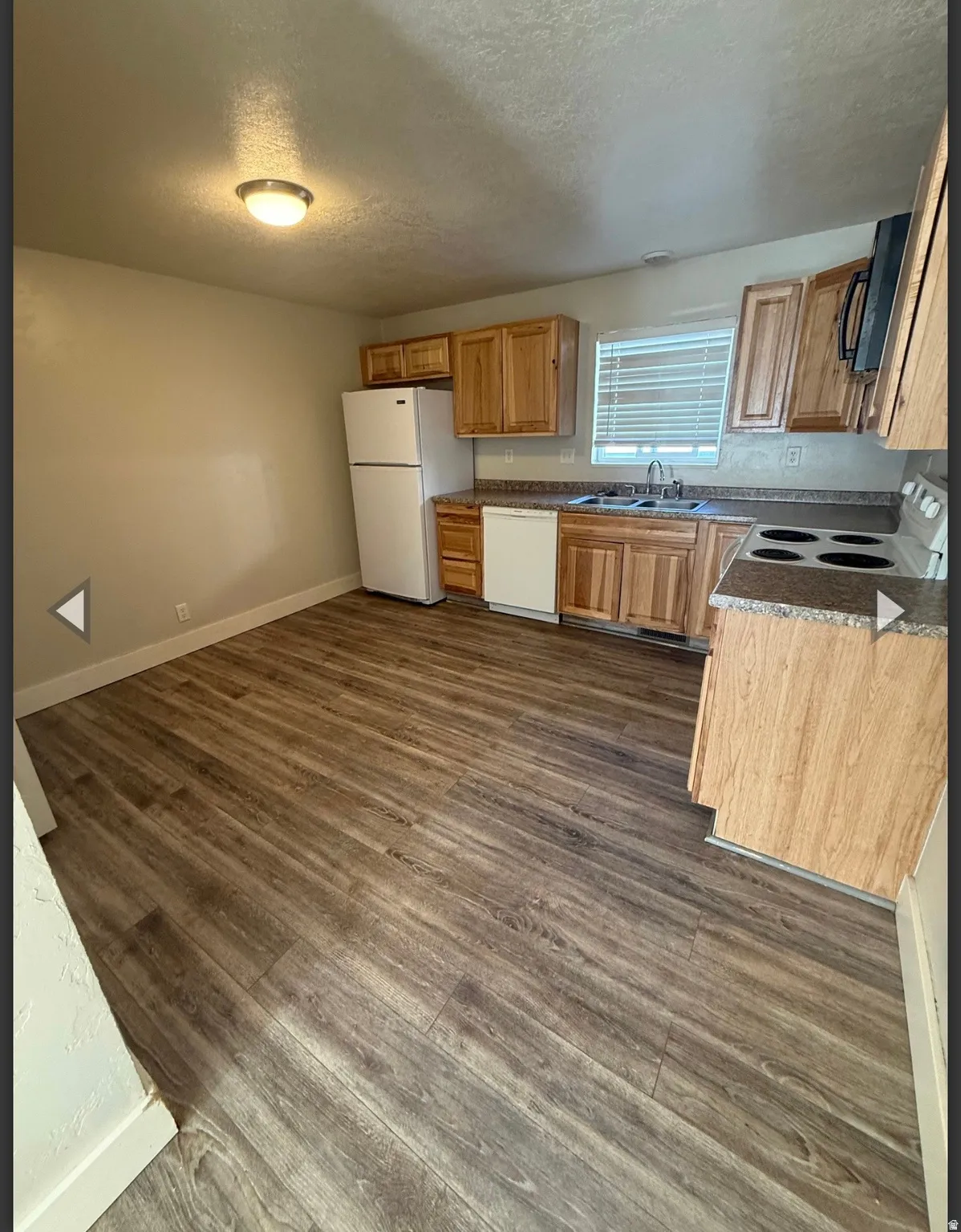 Kitchen with a textured ceiling, white appliances, dark wood-style floors, and wood finish cabinetry